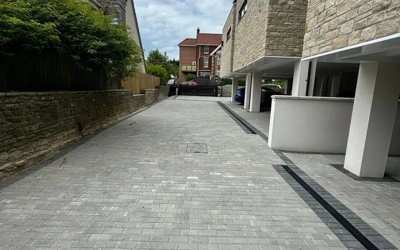 Block-paved parking area with a linear drainage channel running alongside a building