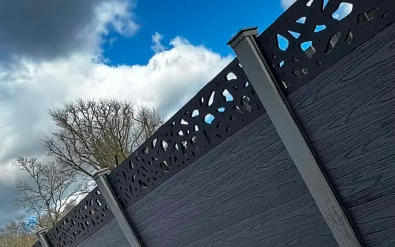 Dark grey composite fence panels with decorative laser-cut tops against a blue sky