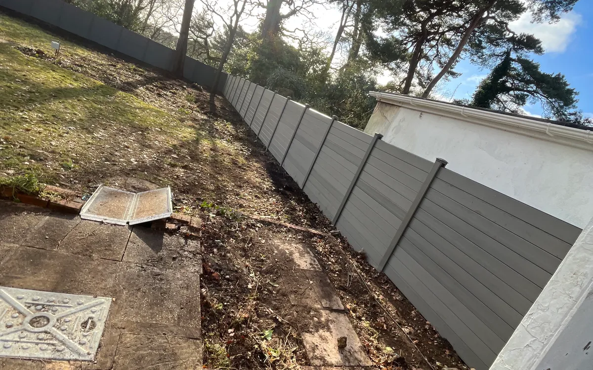 Newly installed grey composite fence panels running the length of a garden boundary