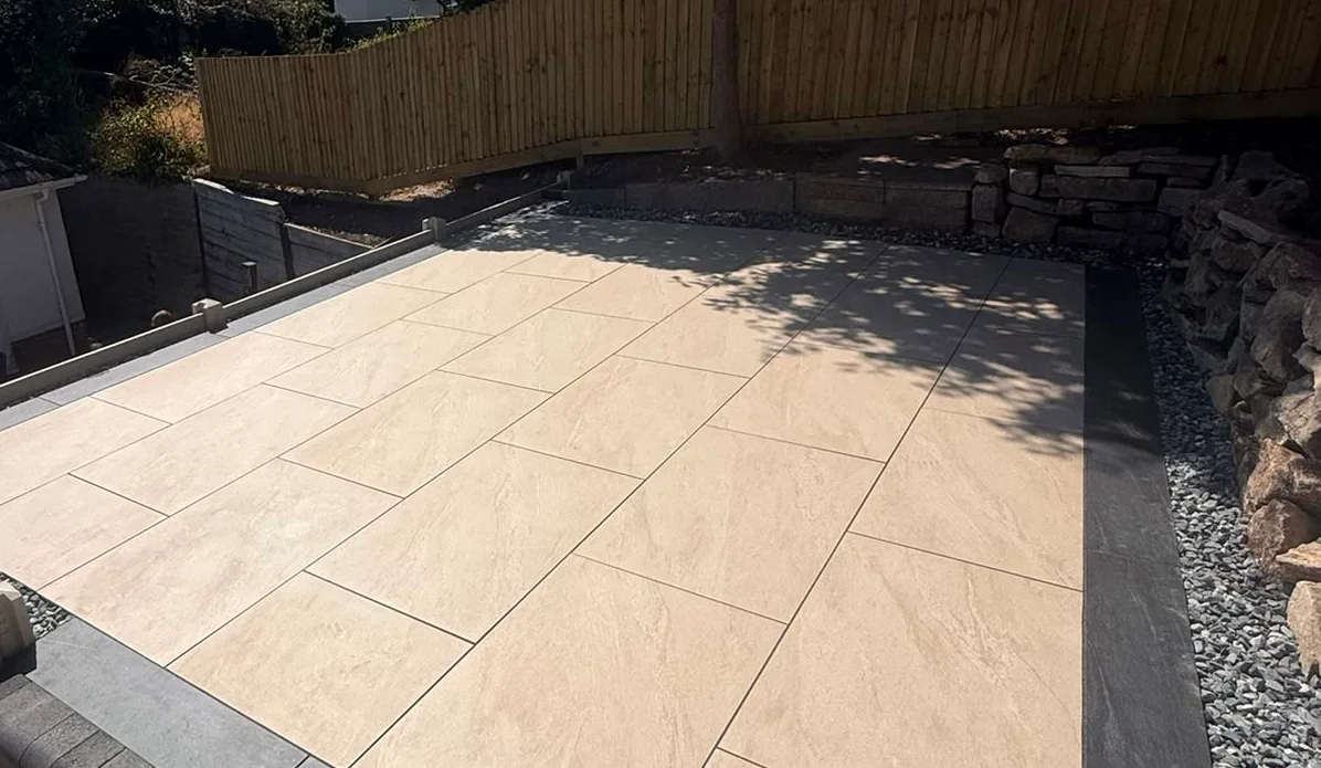 Porcelain paved patio with a charcoal stone border and step, edged with gravel and new closeboard fencing