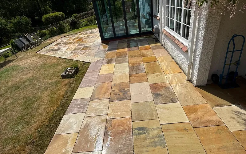 Riven sandstone paving wrapping around the corner of a house onto a lawn
