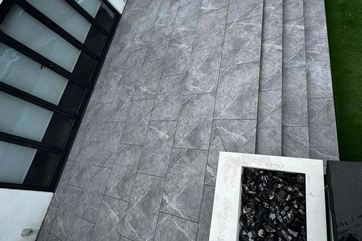 Grey porcelain paving with a wide step down to a lower terrace, edged with dark setts