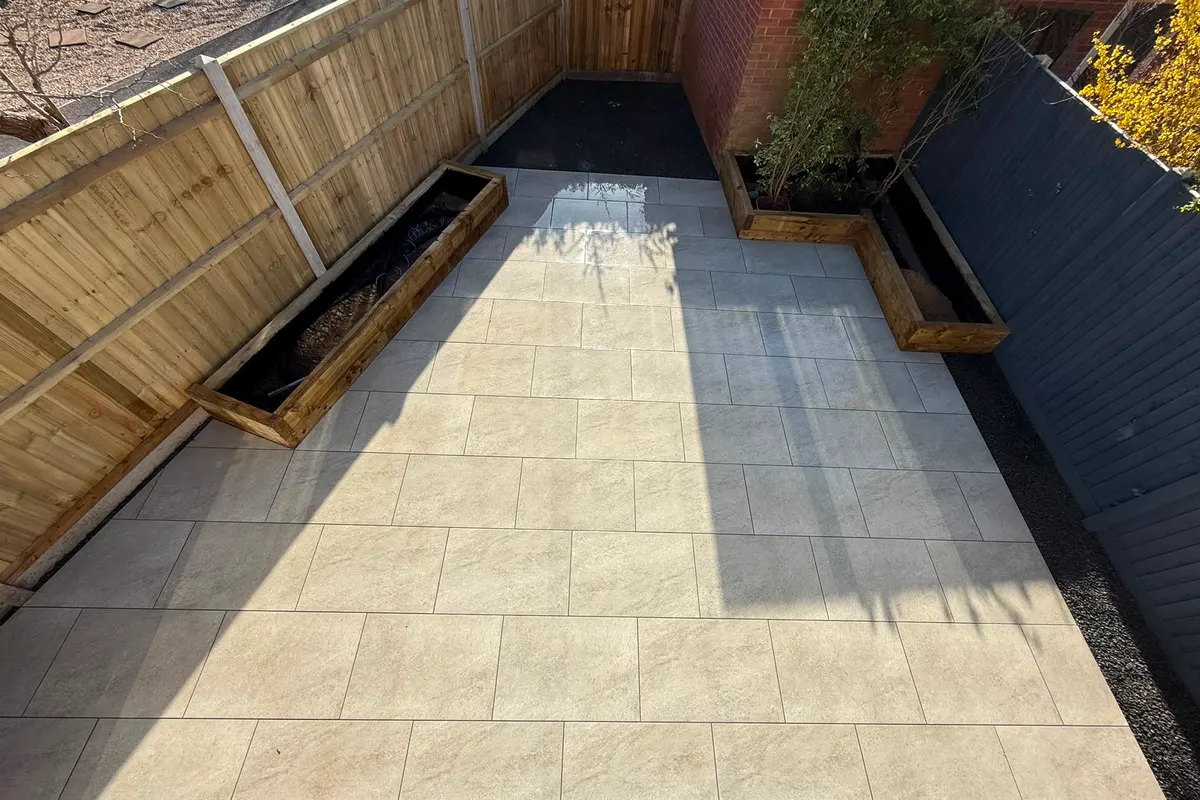 Grey porcelain patio with wide steps and a gravel border between a house and a fence line